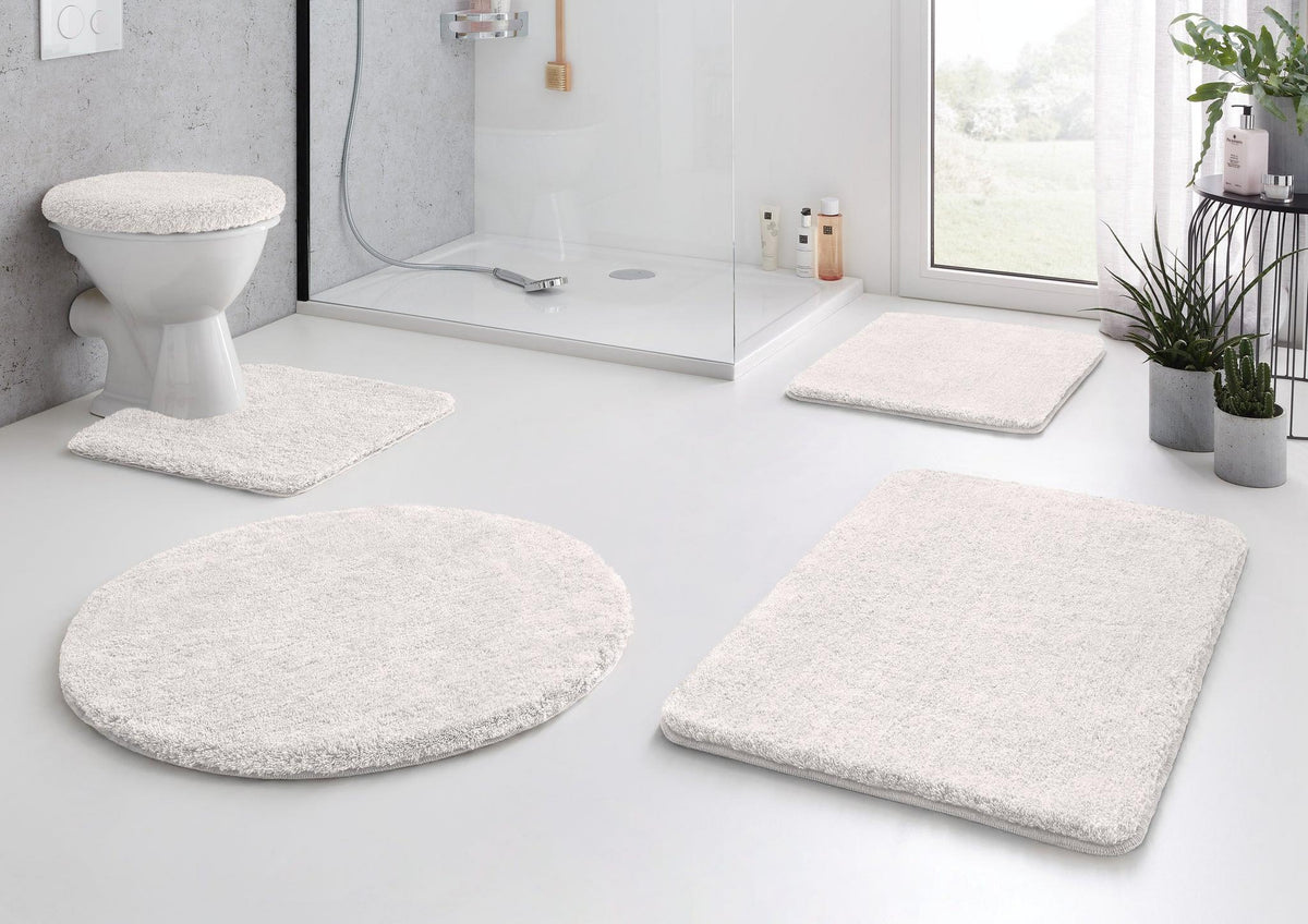 Weißes Bad-Set mit Teppichen vor Dusche, WC und Waschbecken im hellen Bad