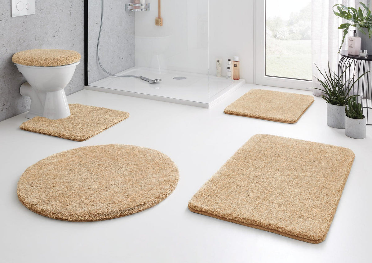Beiges Badteppich-Set vor Dusche und WC auf weißem Badezimmerboden