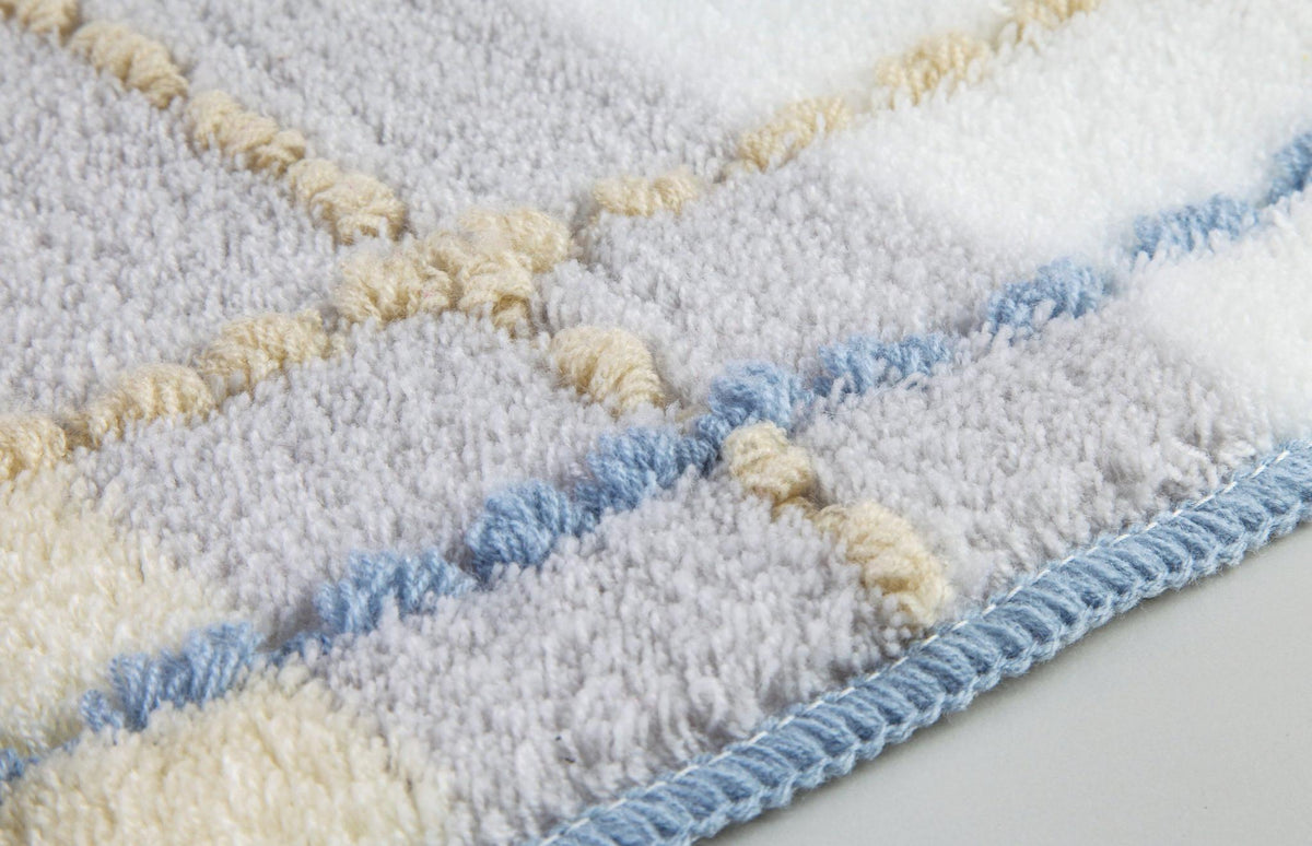 Nahaufnahme weicher Badematte mit kariertem Muster in Grau, Beige, Blau