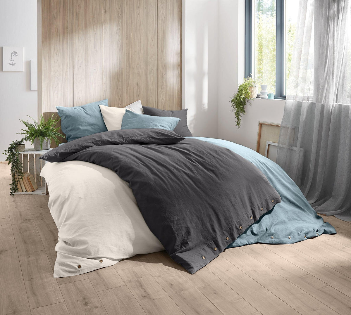 Modernes Bett mit grauer, blauer und weißer Bettwäsche am Fenster