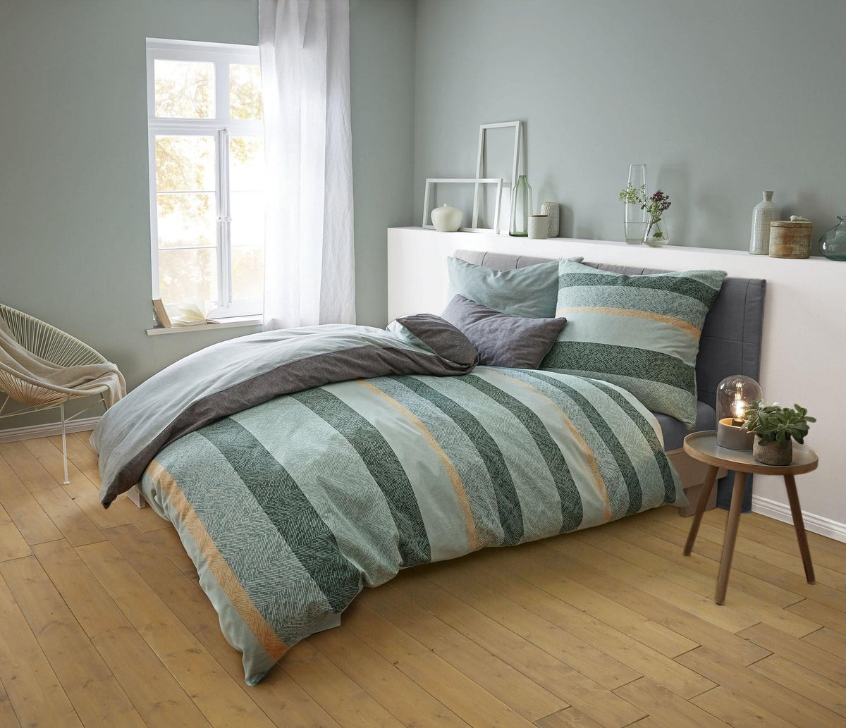 Modernes Schlafzimmer mit grün gestreifter Bettwäsche und Deko auf Ablage