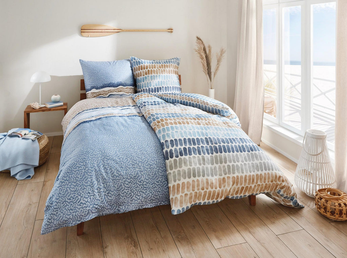 Helles Schlafzimmer mit Holzbett und blau gemusterter Bettwäsche und Kissen