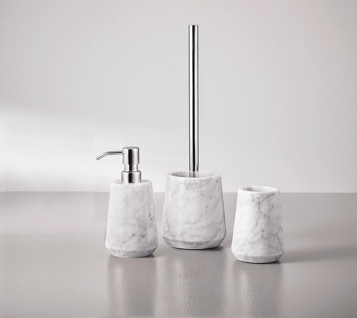 Drei weiße Marmor-Badaccessoires: Seifenspender, Becher, WC-Bürste