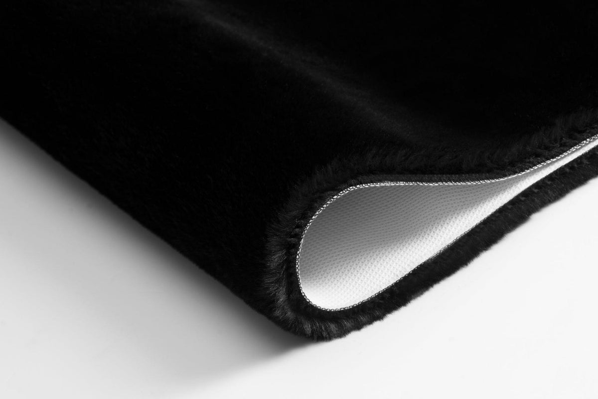 Nahaufnahme einer schwarzen, flauschigen Badematte mit weißer Unterseite