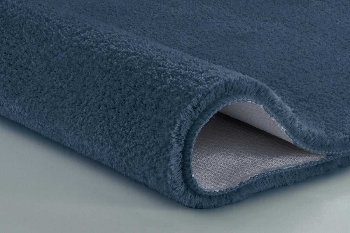 Nahaufnahme einer dunkelblauen, flauschigen Badematte, aufgerollte Kante