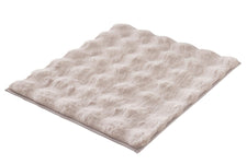 Beige, flauschige Badematte mit Wellenstruktur auf weißem Hintergrund