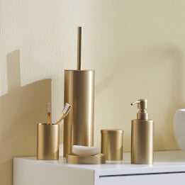 Goldfarbenes Accessoire-Set mit Seifenspender, Becher und Bürste. 
