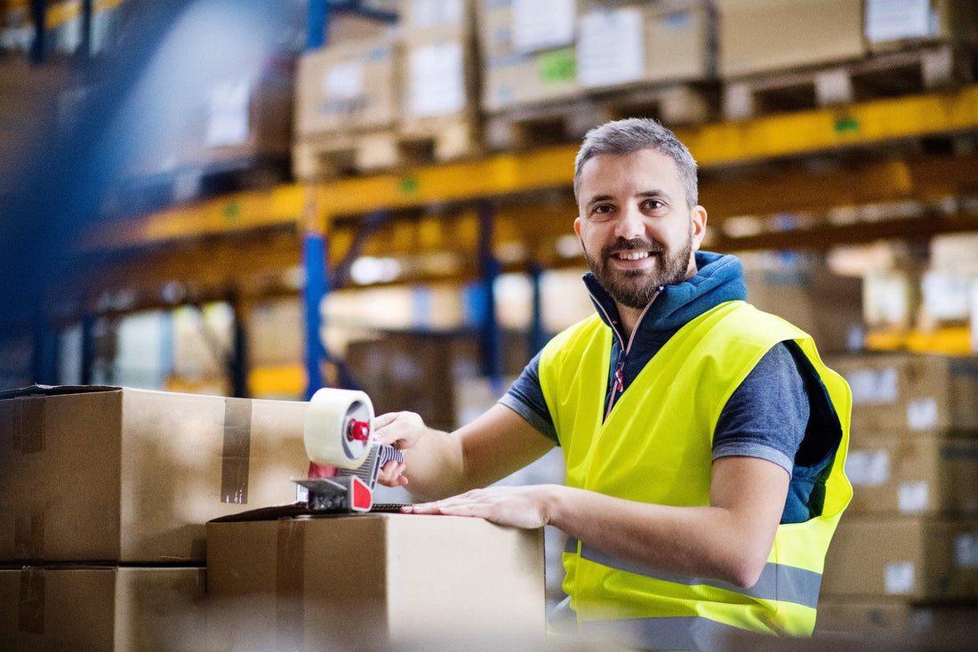 Mitarbeiter im Lager verpackt Kartons mit Paketband an einem Tisch