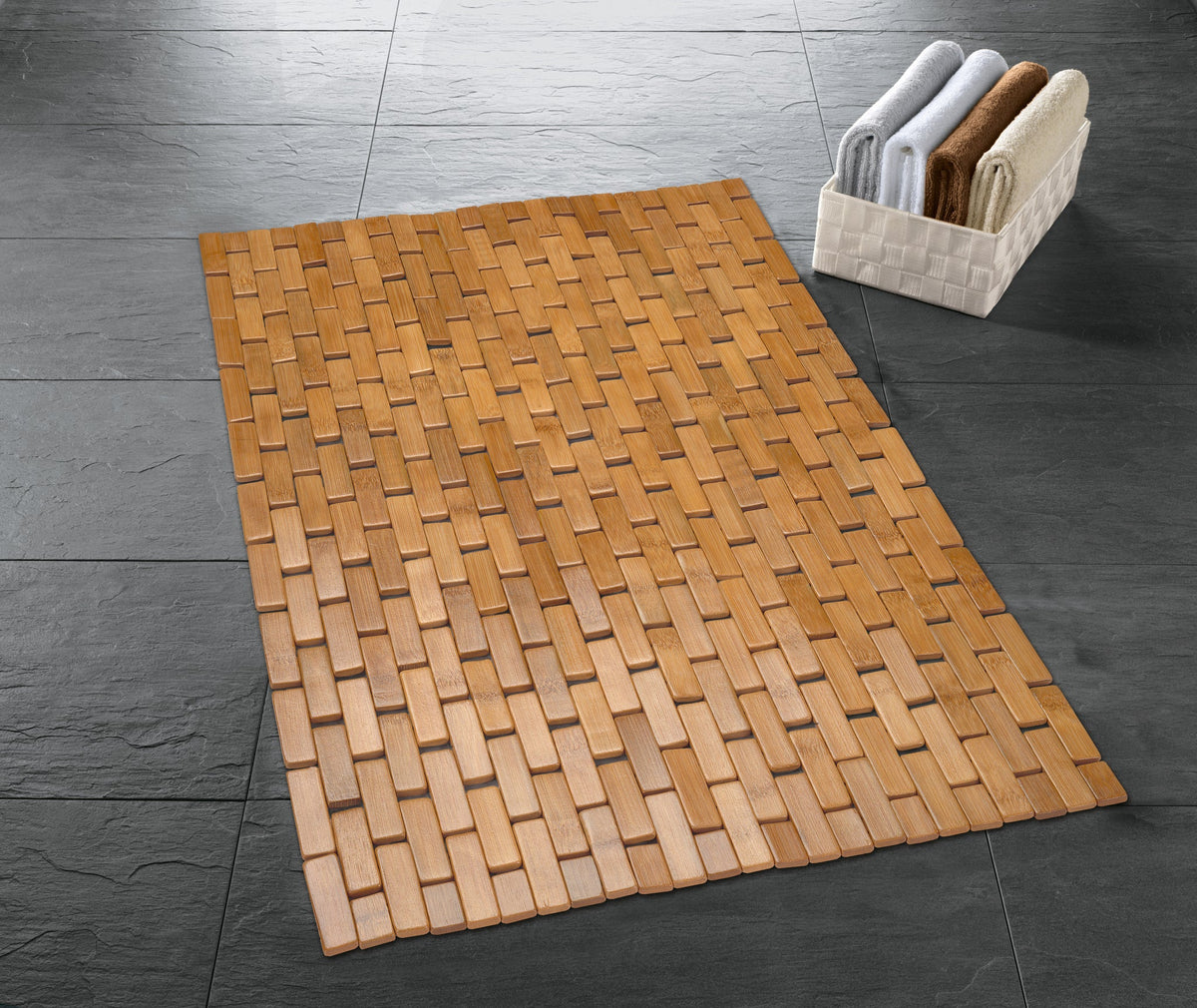Holz-Badematte auf dunklem Fliesenboden neben kleinem weißen Korb mit Handtüchern