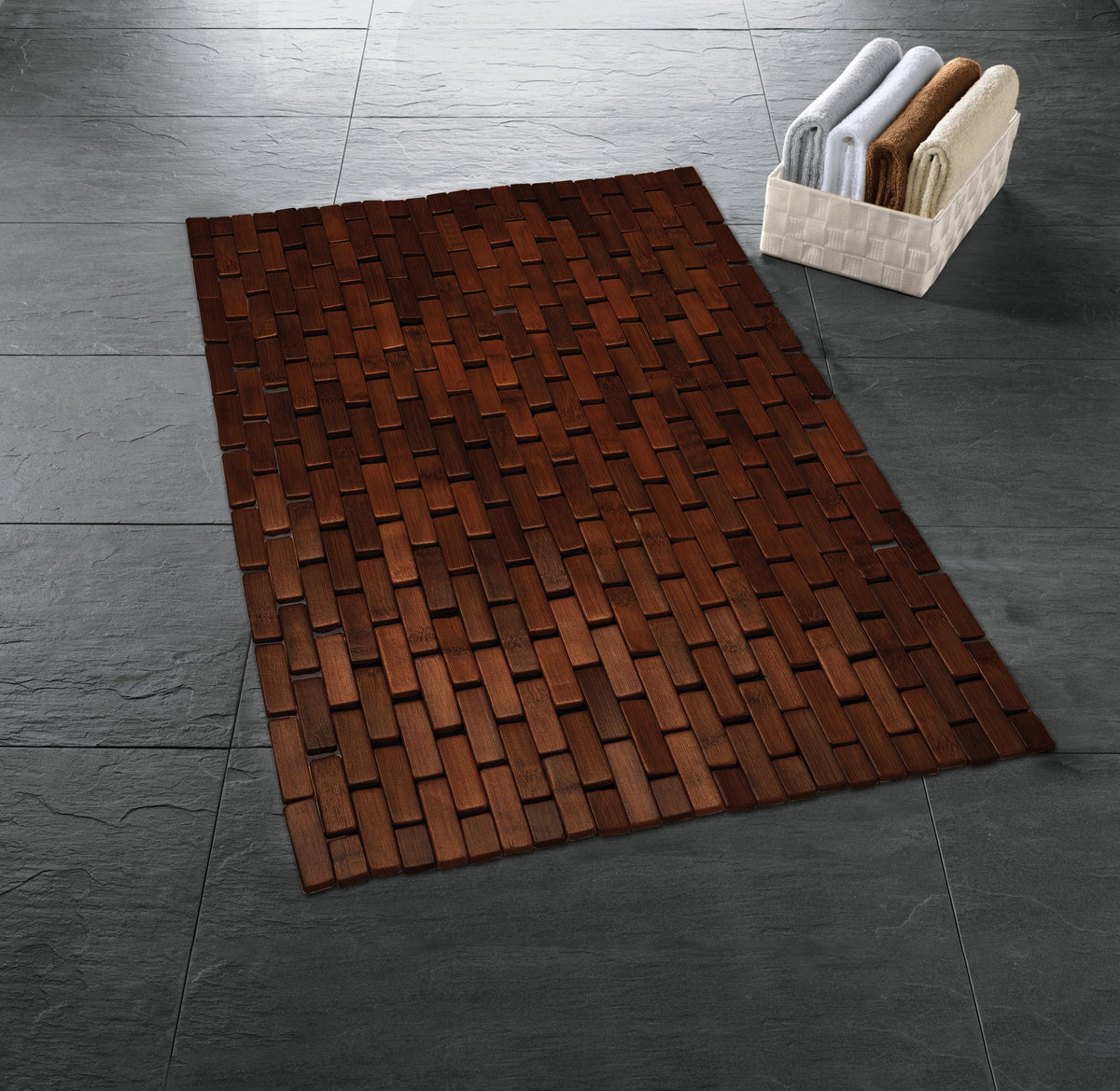 Dunkle Holz-Badematte auf grauem Fliesenboden neben weißem Handtuchkorb