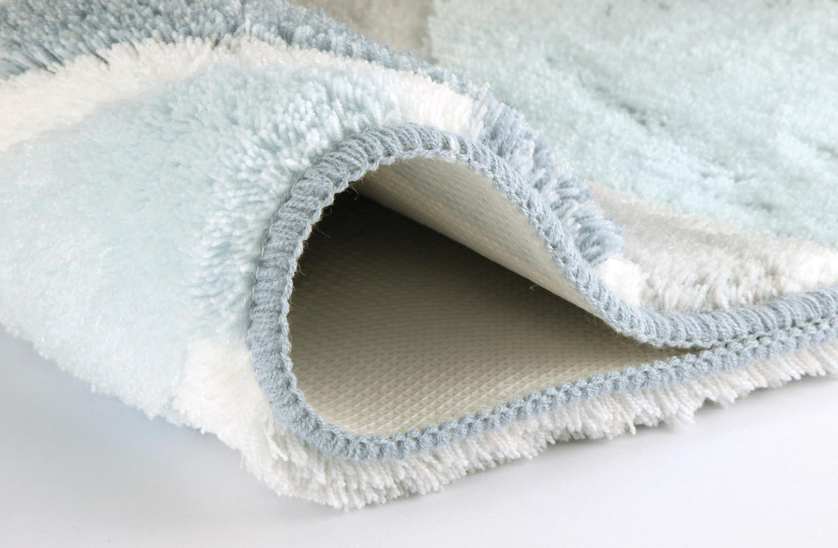 Weißer Badteppich mit hellblauer Umrandung, umgeschlagen im Detail.