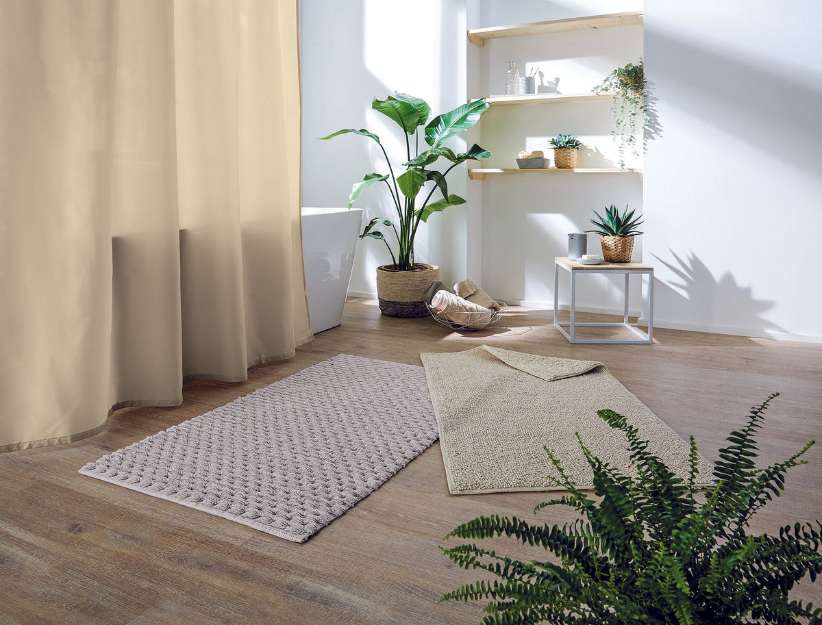 Zwei beige Badematten auf Holzfußboden mit Pflanzen und Regal im hellen Bad