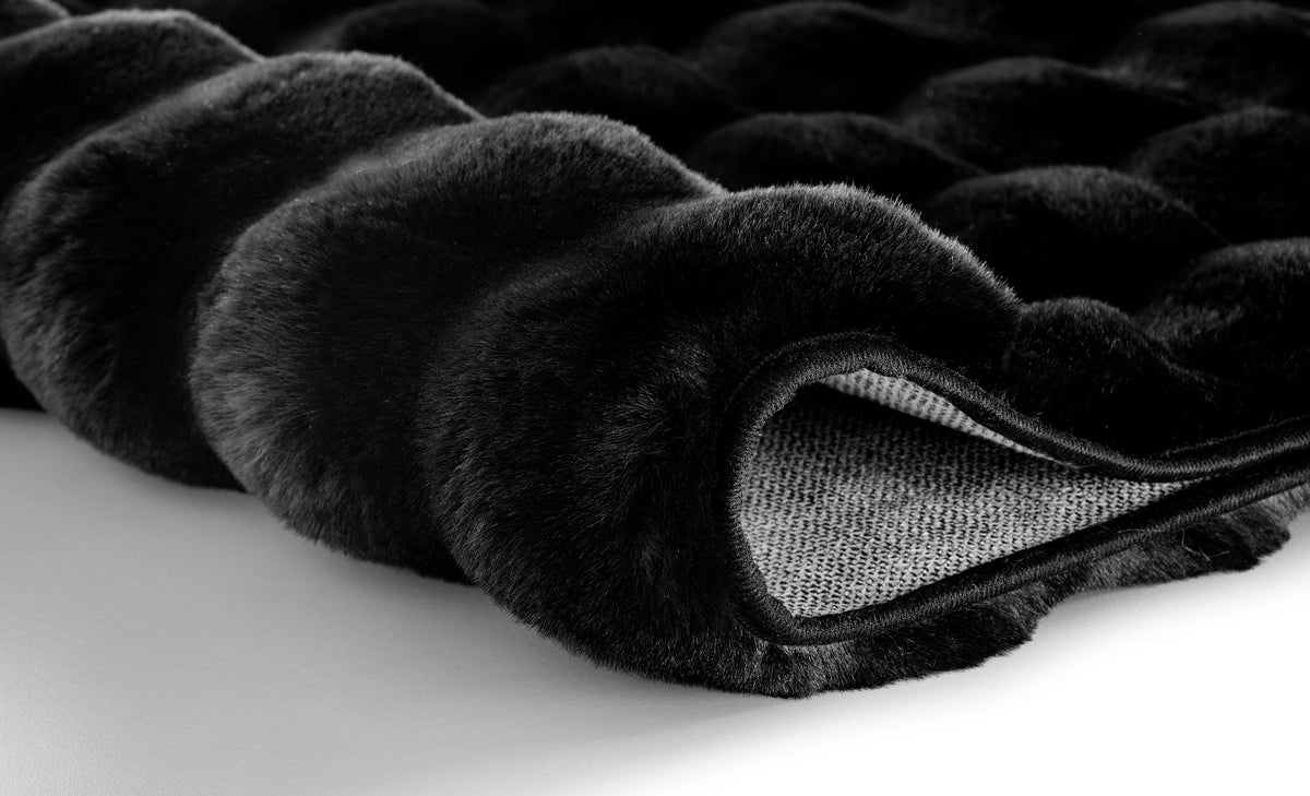 Schwarzer, flauschiger Badezimmerteppich in Nahaufnahme, gerollte Kante