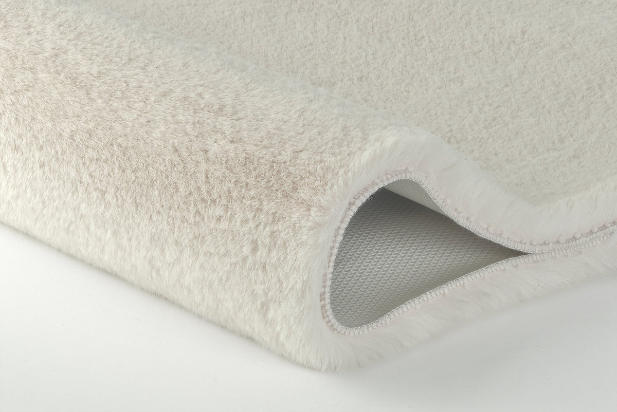 Nahaufnahme einer beige-weißen, flauschigen Badematte mit abgerundetem Rand