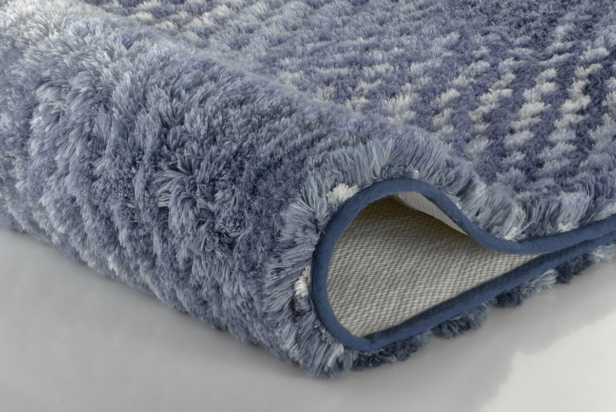 Detailansicht eines flauschigen blau-gemusterten Badteppichs mit Kante