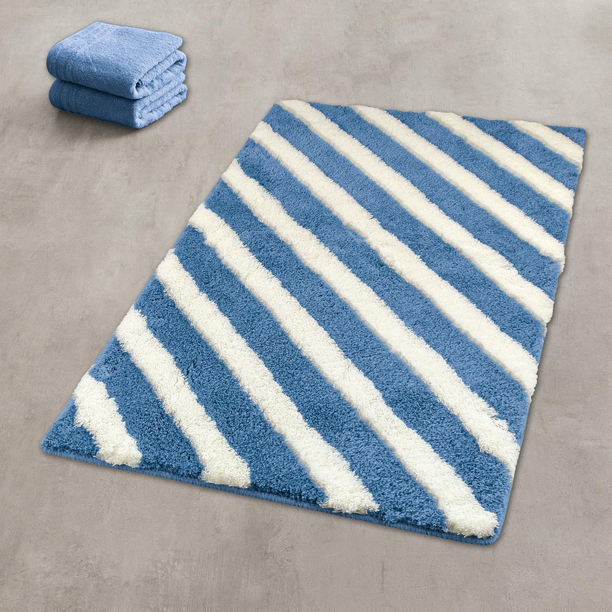 Blau-weißer Badteppich mit diagonalen Streifen, daneben zwei Handtücher.