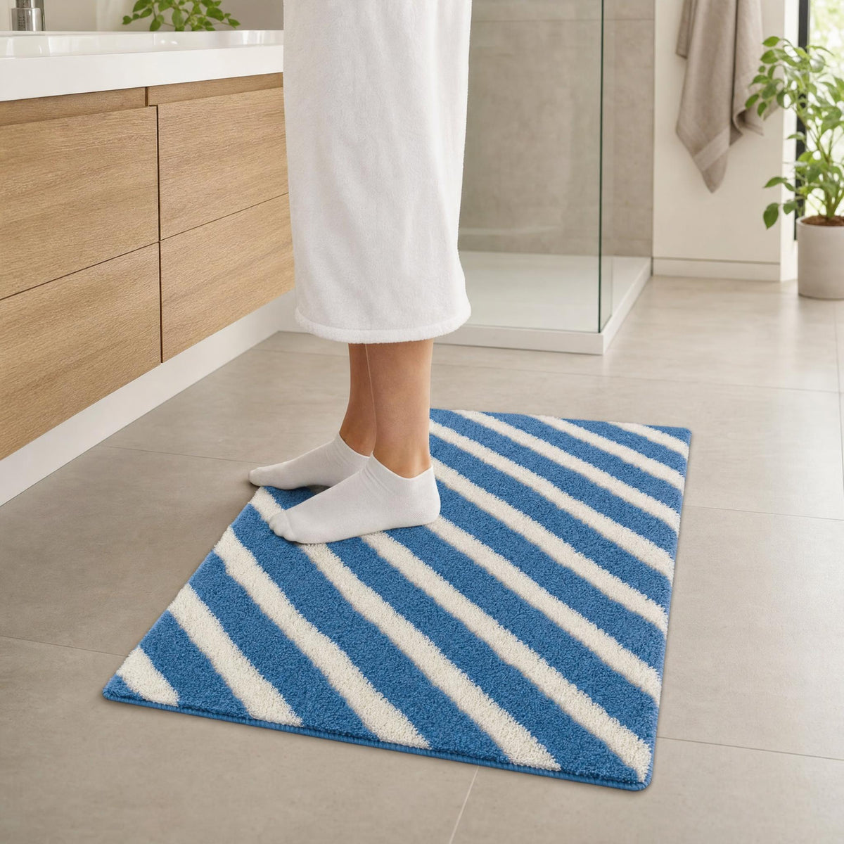 Person im Bad auf blau-weiß gestreifter Badematte vor der Dusche.