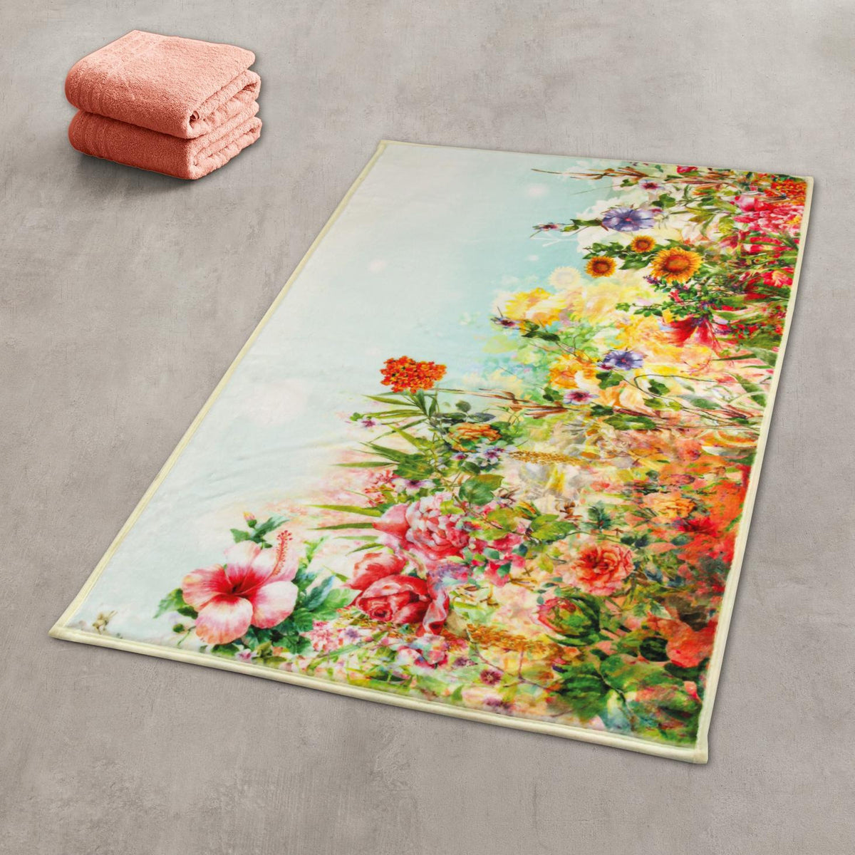 Bunter Badteppich mit Blumenmotiv auf grauem Boden neben rosa Handtüchern.