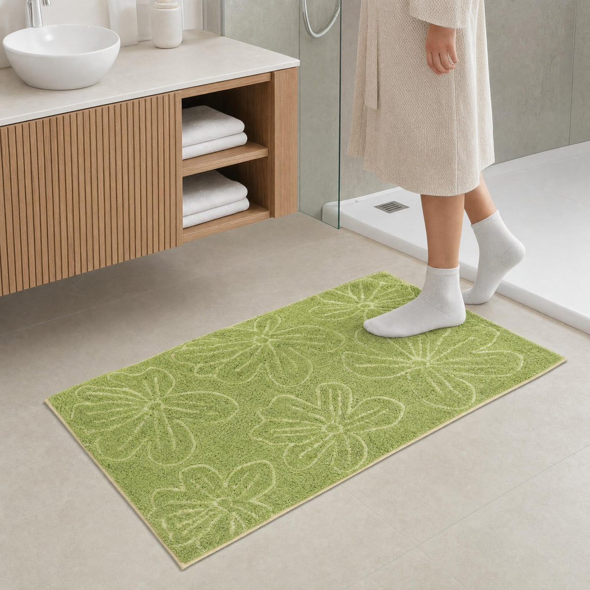 Grüne Badematte mit Blumenmuster vor Dusche und Holzwaschtisch.