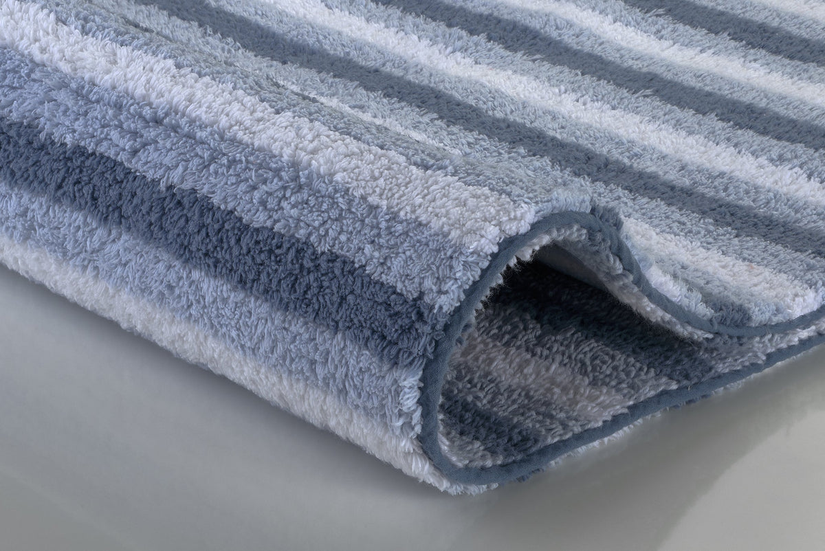 Grau-blau gestreifte, flauschige Badematte auf hellem Untergrund
