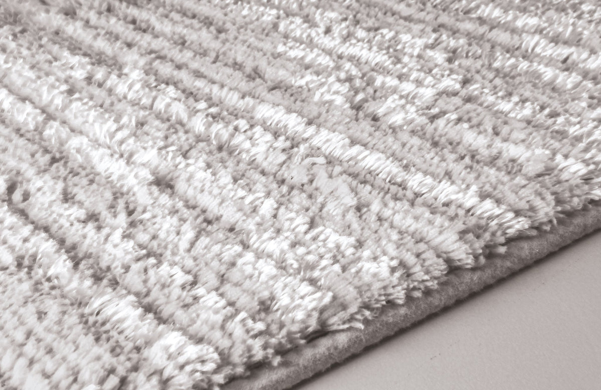 Nahaufnahme einer hellgrauen, hochflorigen Badematte mit weicher Struktur