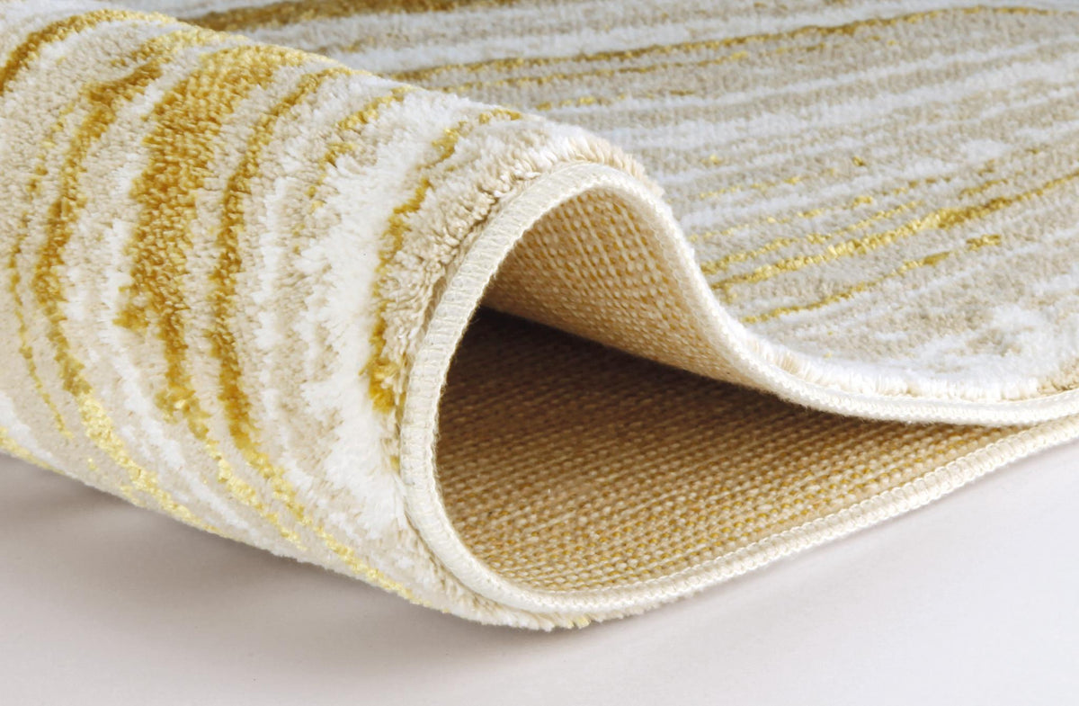 Teilaufgerollter cremeweißer Teppich mit goldfarbigen Wellenmustern.