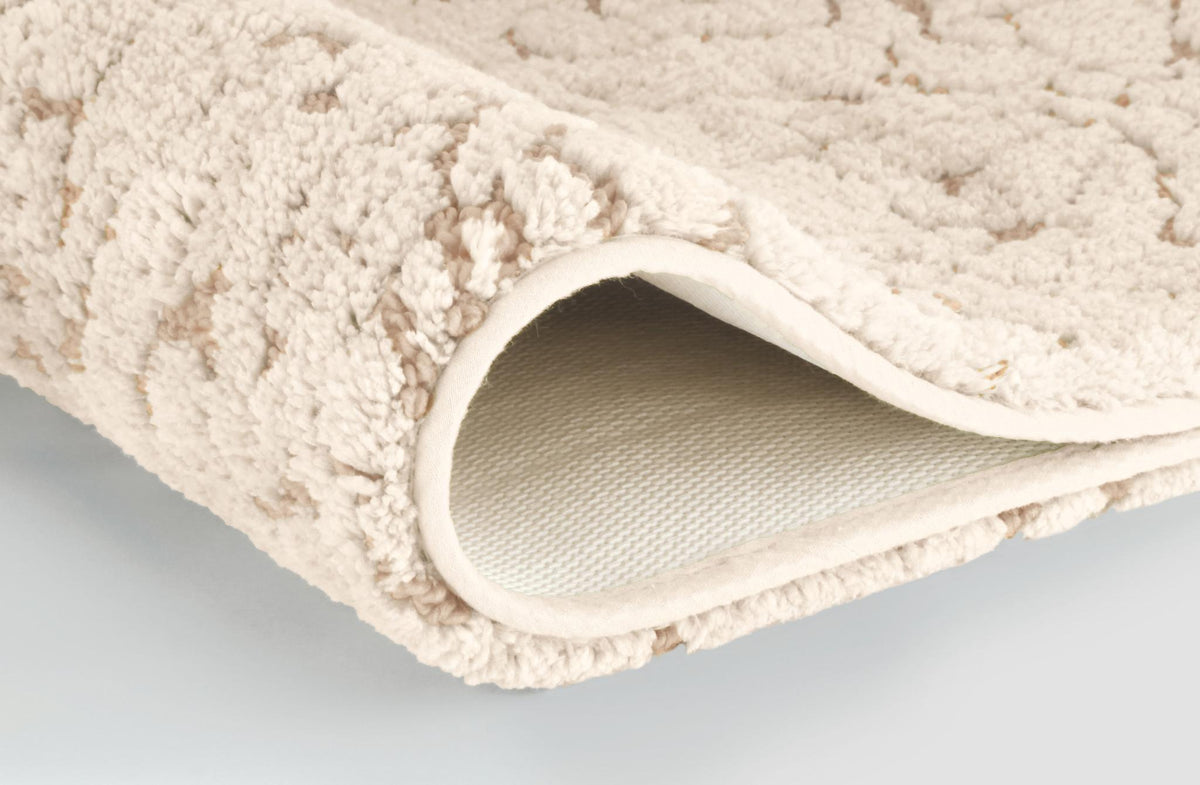 Cremefarbiger Badteppich mit strukturierter Oberfläche und umgeschlagener Ecke.