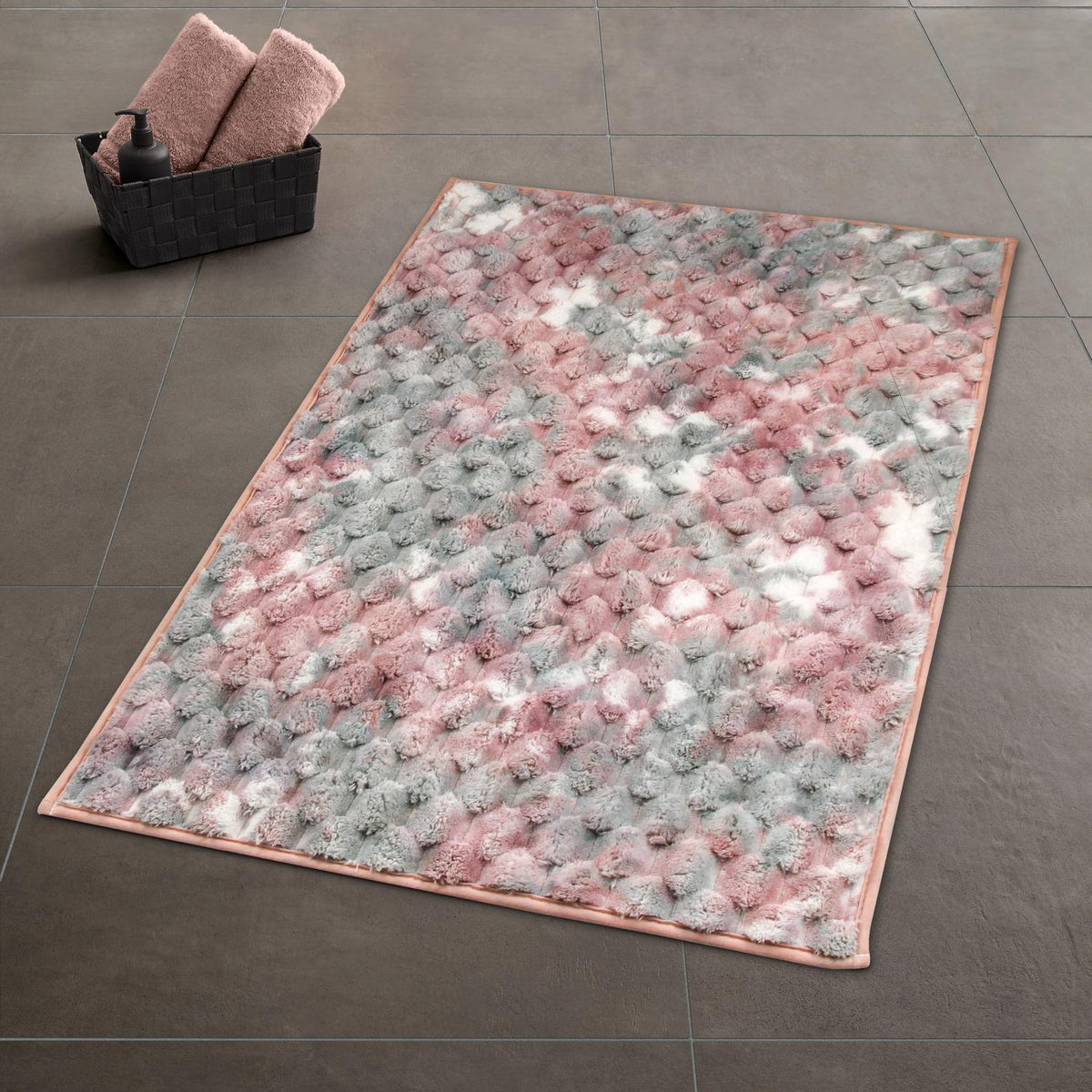 Flauschiger Badteppich in Rosa, Grau und Weiß auf dunklen Fliesen.