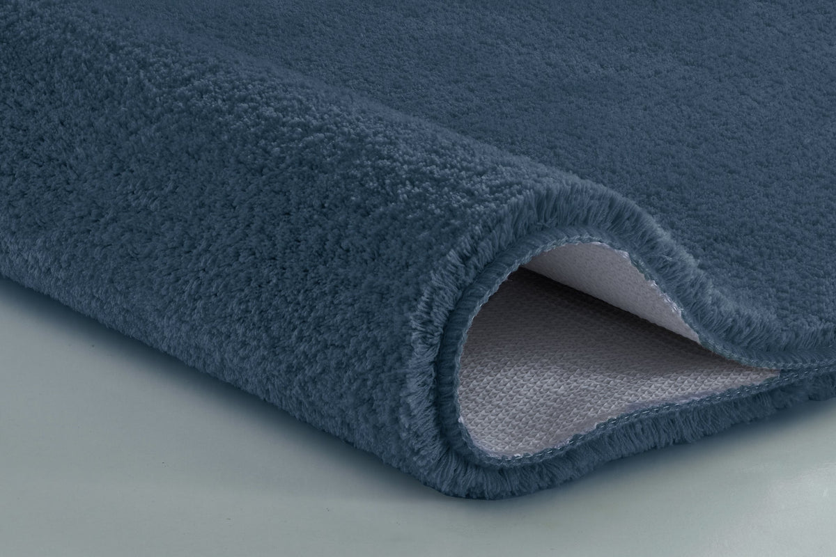 Nahaufnahme einer gerollten, dunkelblauen Badematte mit Flauschflor