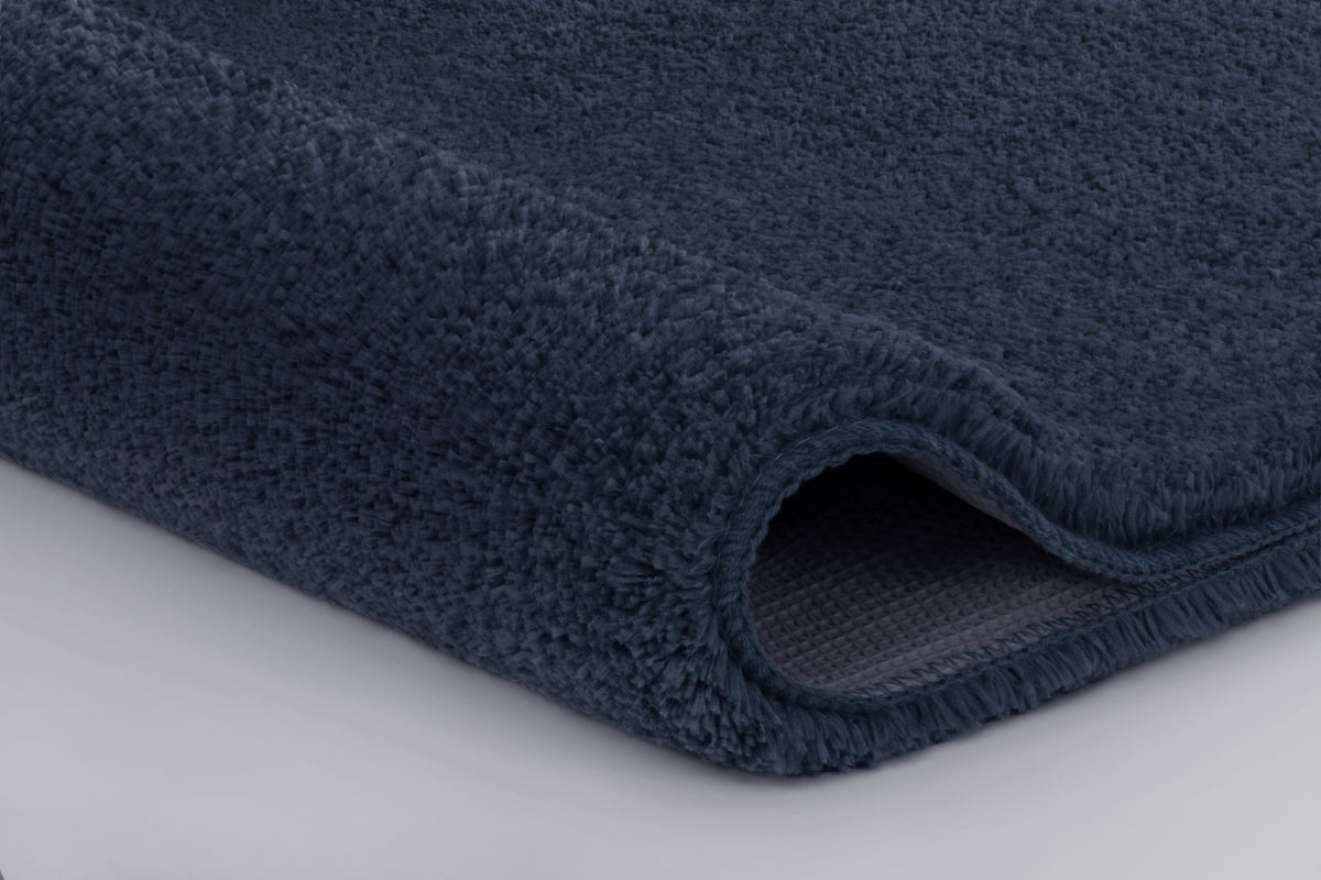 Dunkelblauer, flauschiger Badteppich in Nahaufnahme mit gerollter Kante