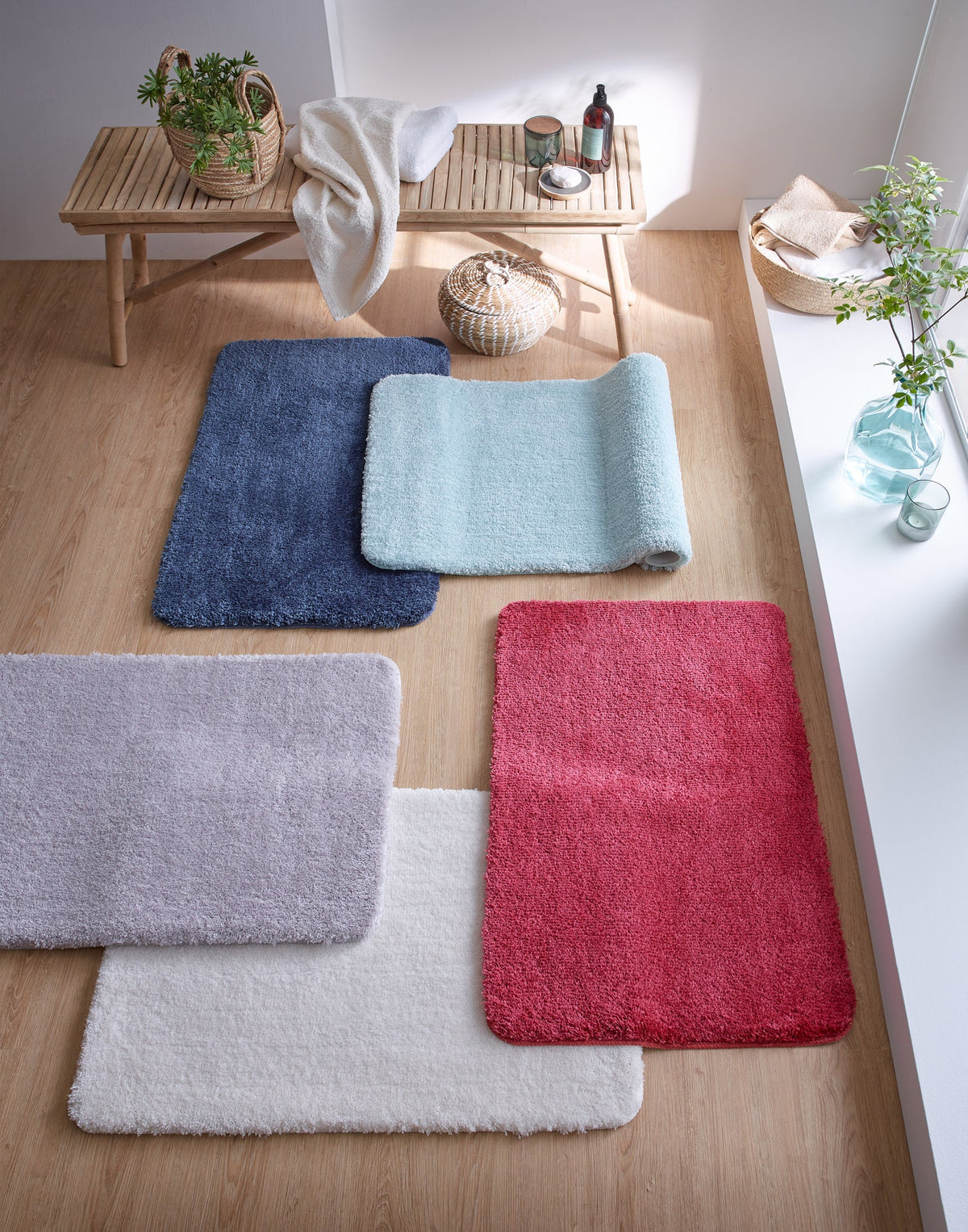 Flauschige Badematten in Blau, Mint, Grau, Rot und Weiß auf Holzboden