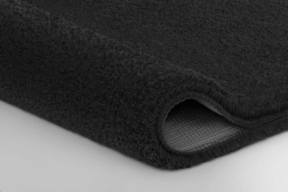 Nahaufnahme einer gefalteten dunkelgrauen Badematte mit Flauschkante