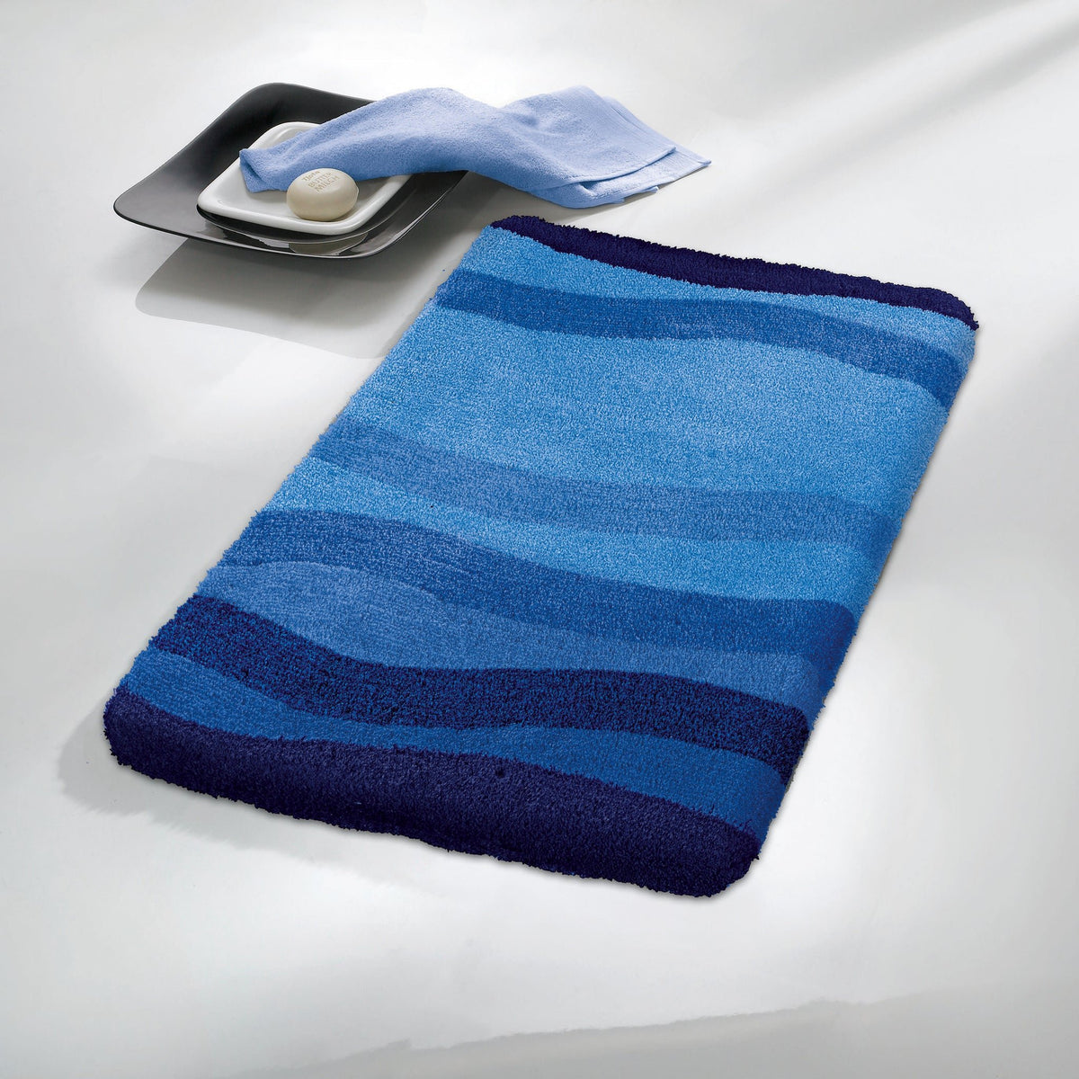 Blauer Badematte mit Wellenmuster, daneben Seife und kleines Handtuch