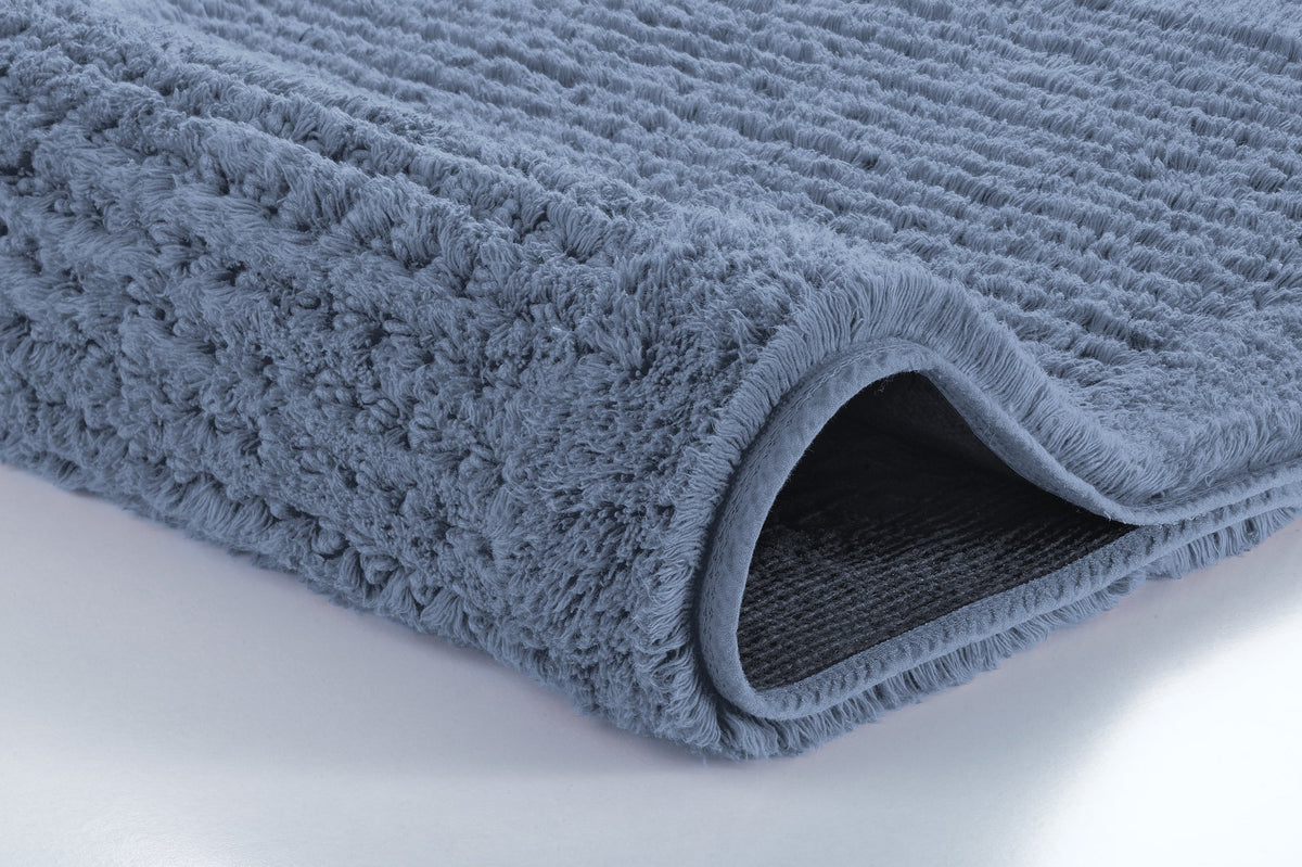Nahaufnahme einer gefalteten, flauschigen blauen Badematte mit Rückseite