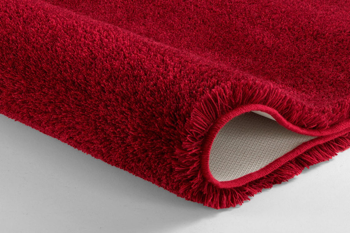 Roter Badteppich in Nahaufnahme mit eingerollter Ecke und Rückseite