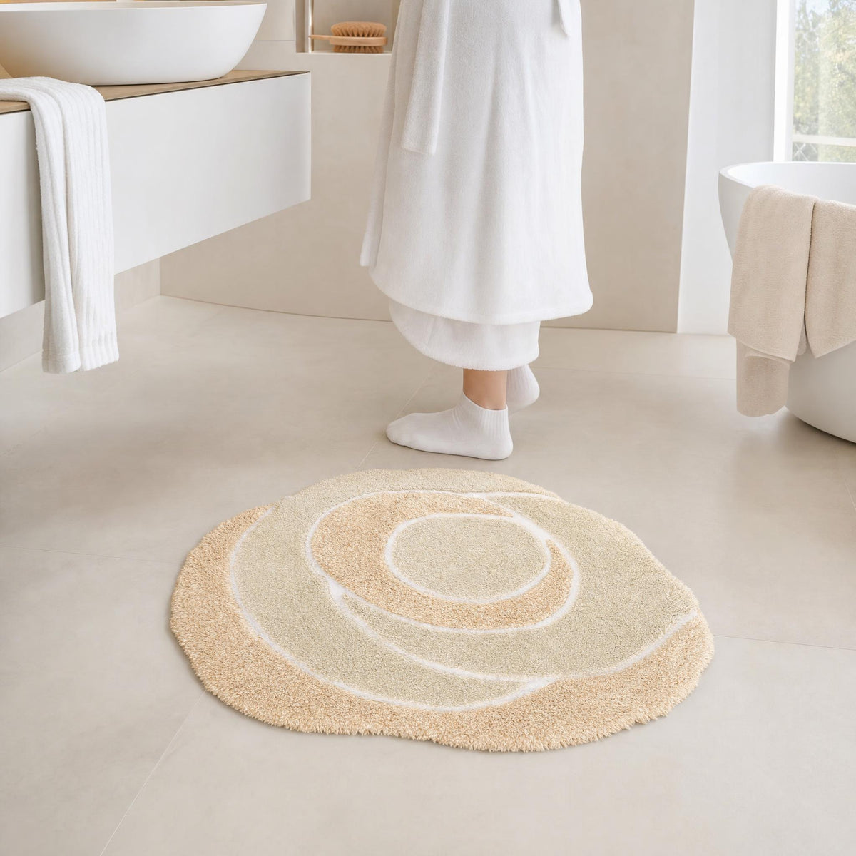 Runder cremefarbener Badteppich in hellem Bad vor Badewanne und Waschtisch.