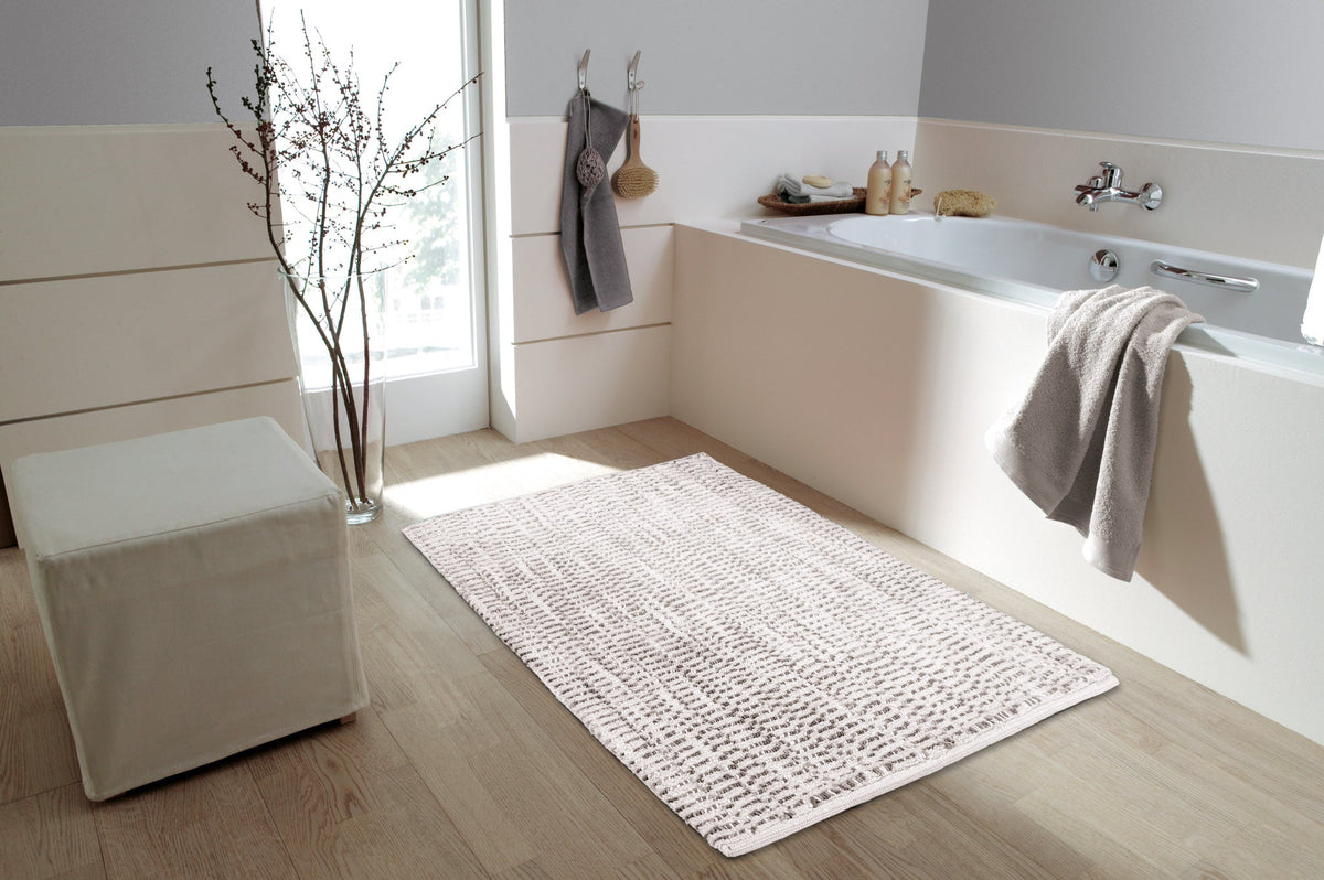 Helles Badezimmer mit Badewanne, cremefarbenem Badteppich und Handtüchern