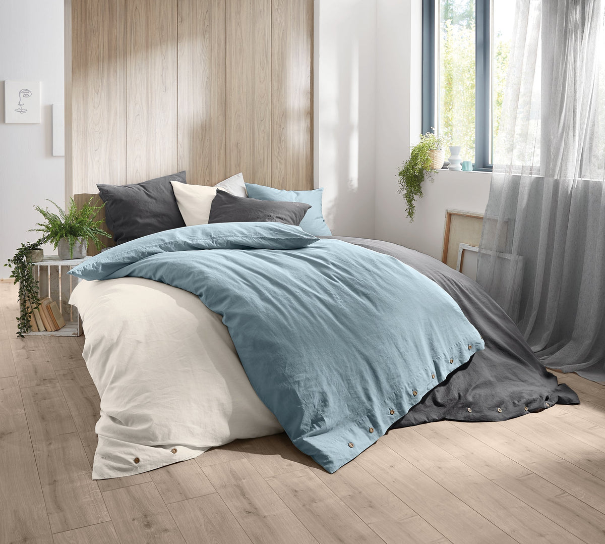 Doppelbett mit blauer, weißer und grauer Bettwäsche im hellen Zimmer