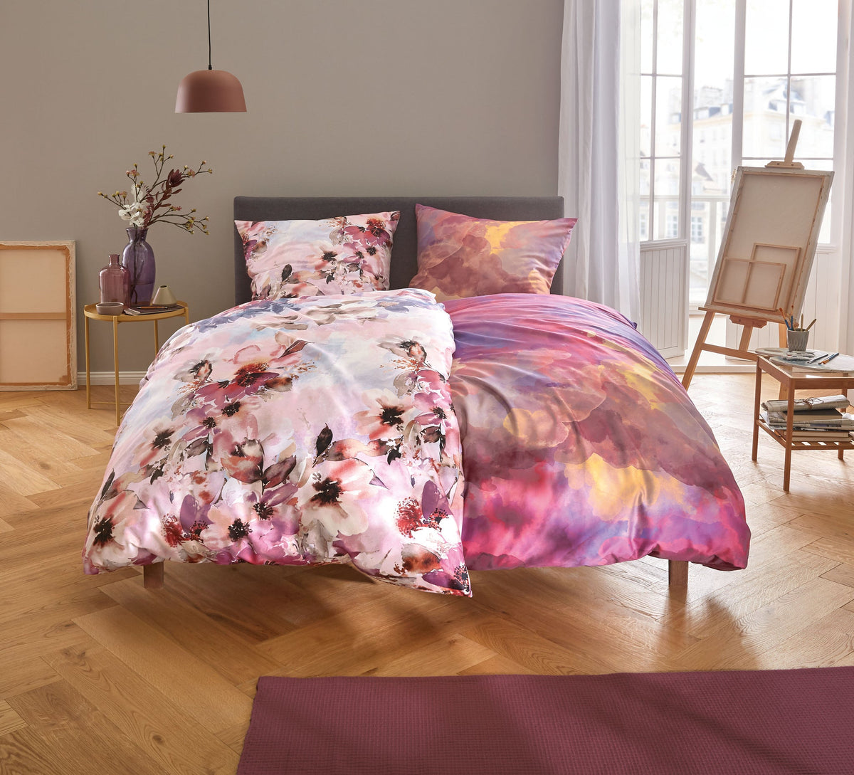 Doppelbett mit bunter Bettwäsche in Rosa-Lila-Tönen und Blumenmuster