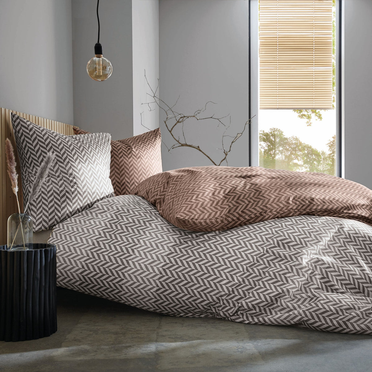 Modernes Bett mit gemusterter Bettwäsche in Braun und Grau am Fenster