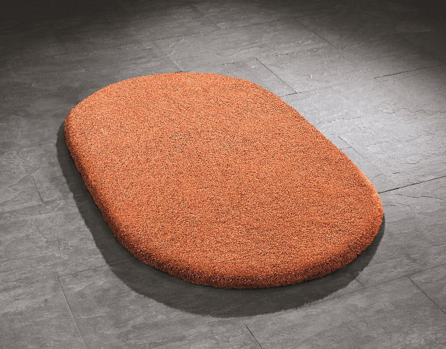Ovaler oranger Badematte aus Hochflor auf grauem Fliesenboden liegend