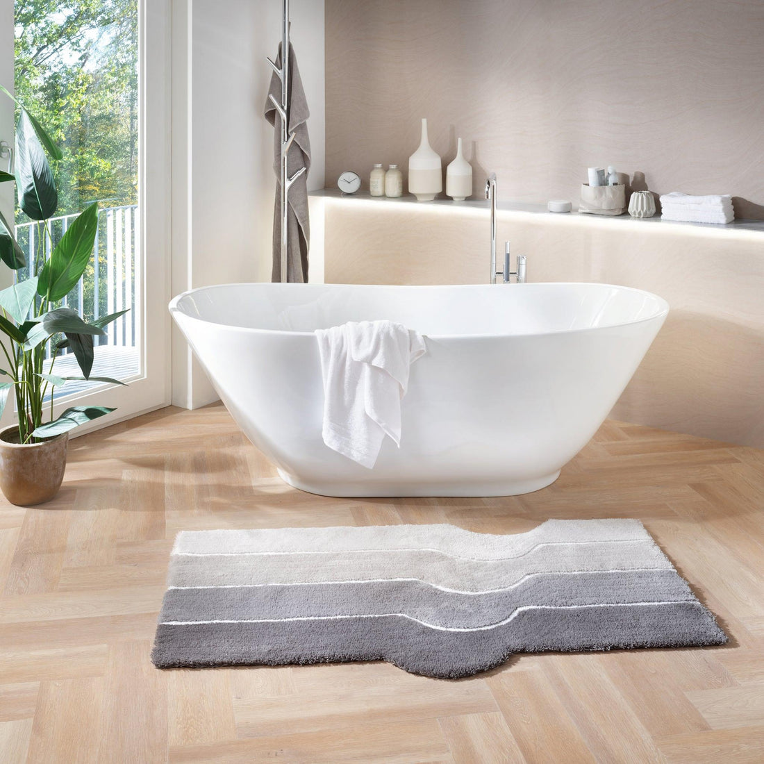 Freistehende weiße Badewanne mit Handtuch und grauem Badteppich davor