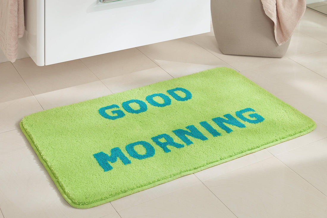 Grüne Badematte mit blauem Schriftzug GOOD MORNING auf Fliesenboden