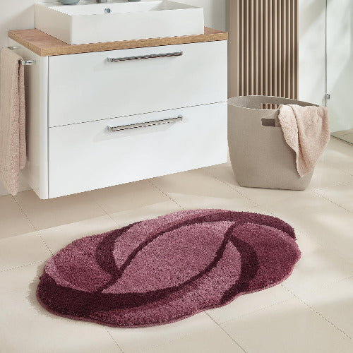 Ovale Badematte in Rosa- und Bordeaux-Tönen vor weißem Waschschrank