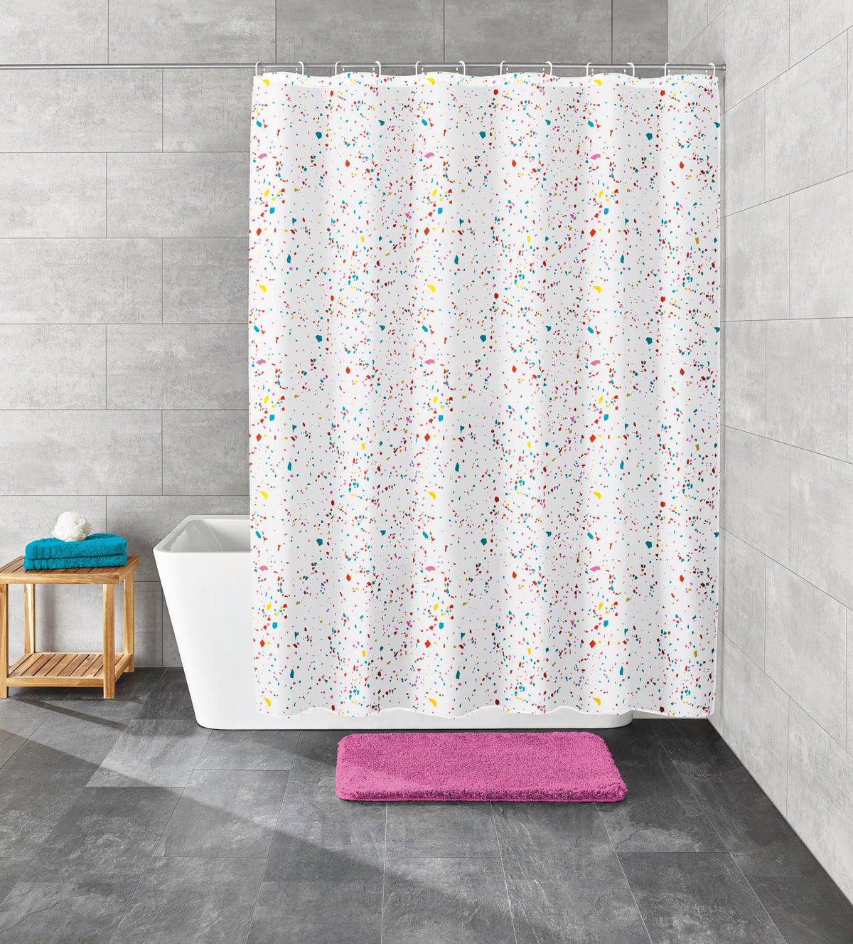 Weiße Badewanne mit buntem Duschvorhang und rosa Badematte auf grauem Fliesenboden