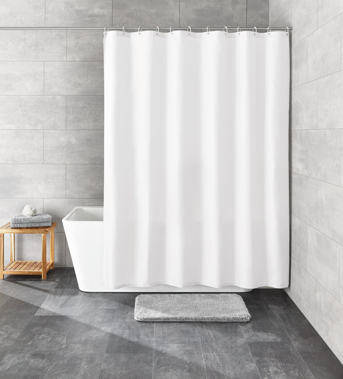 Weißer Duschvorhang an Badewanne mit grauer Matte und kleinem Holzhocker