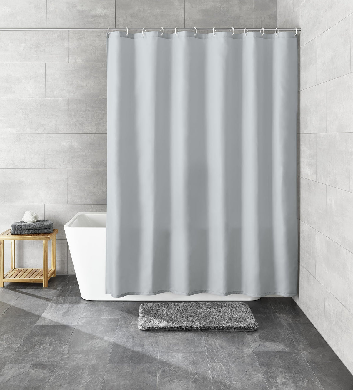 Grauer Duschvorhang vor Badewanne in modern gefliestem Bad, Badteppich