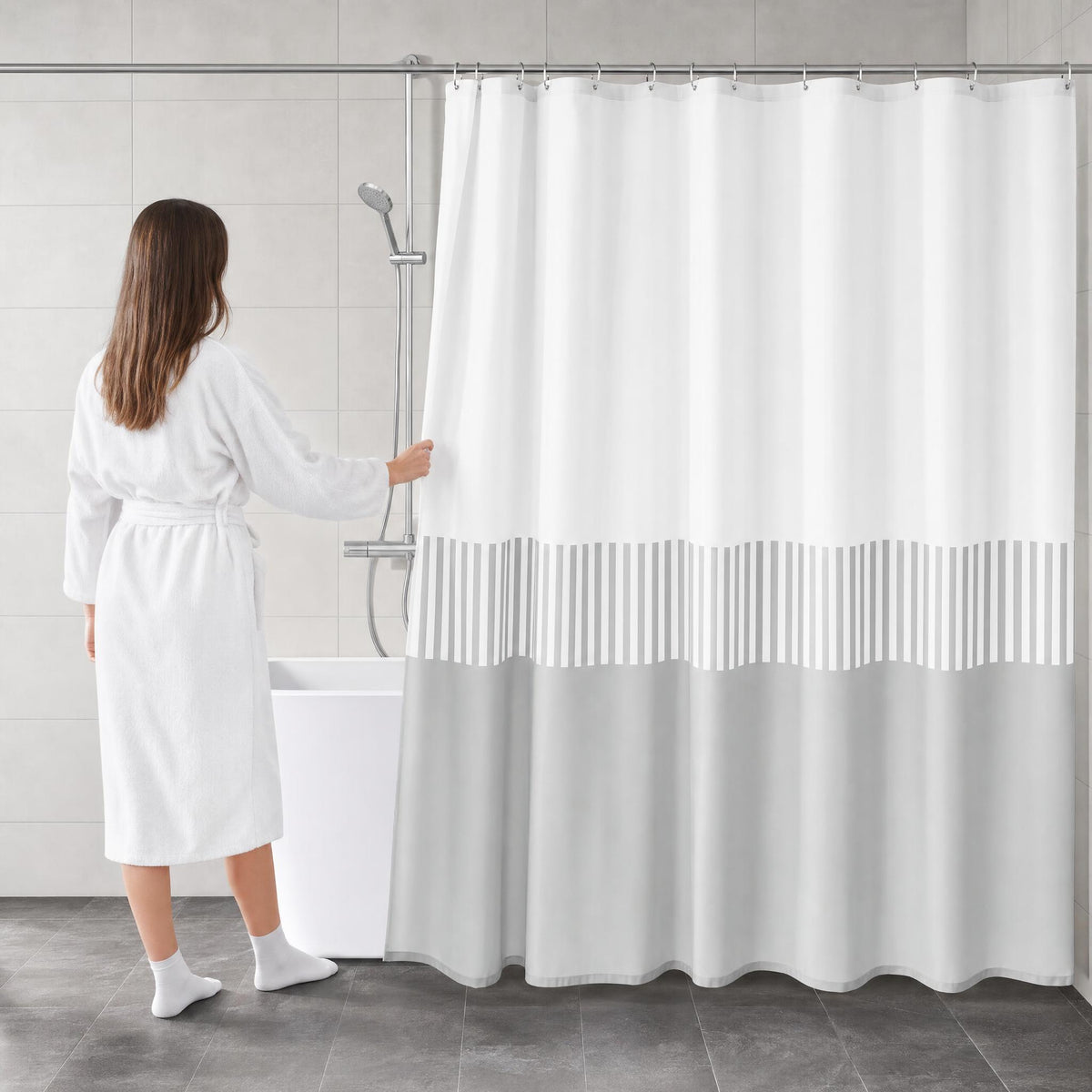Frau im Bademantel zieht einen weiß-grauen Duschvorhang an der Badewanne zu.