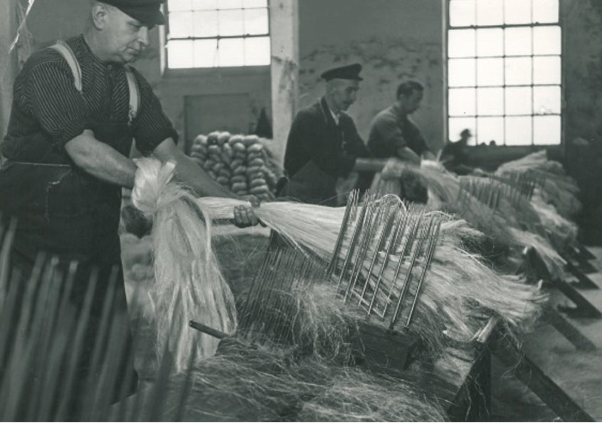 Arbeiter kämmen lange Pflanzenfasern in historischer Fabrikhalle