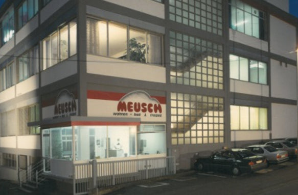 Beleuchtetes Firmengebäude mit MEUSEN-Beschriftung und Parkplatz